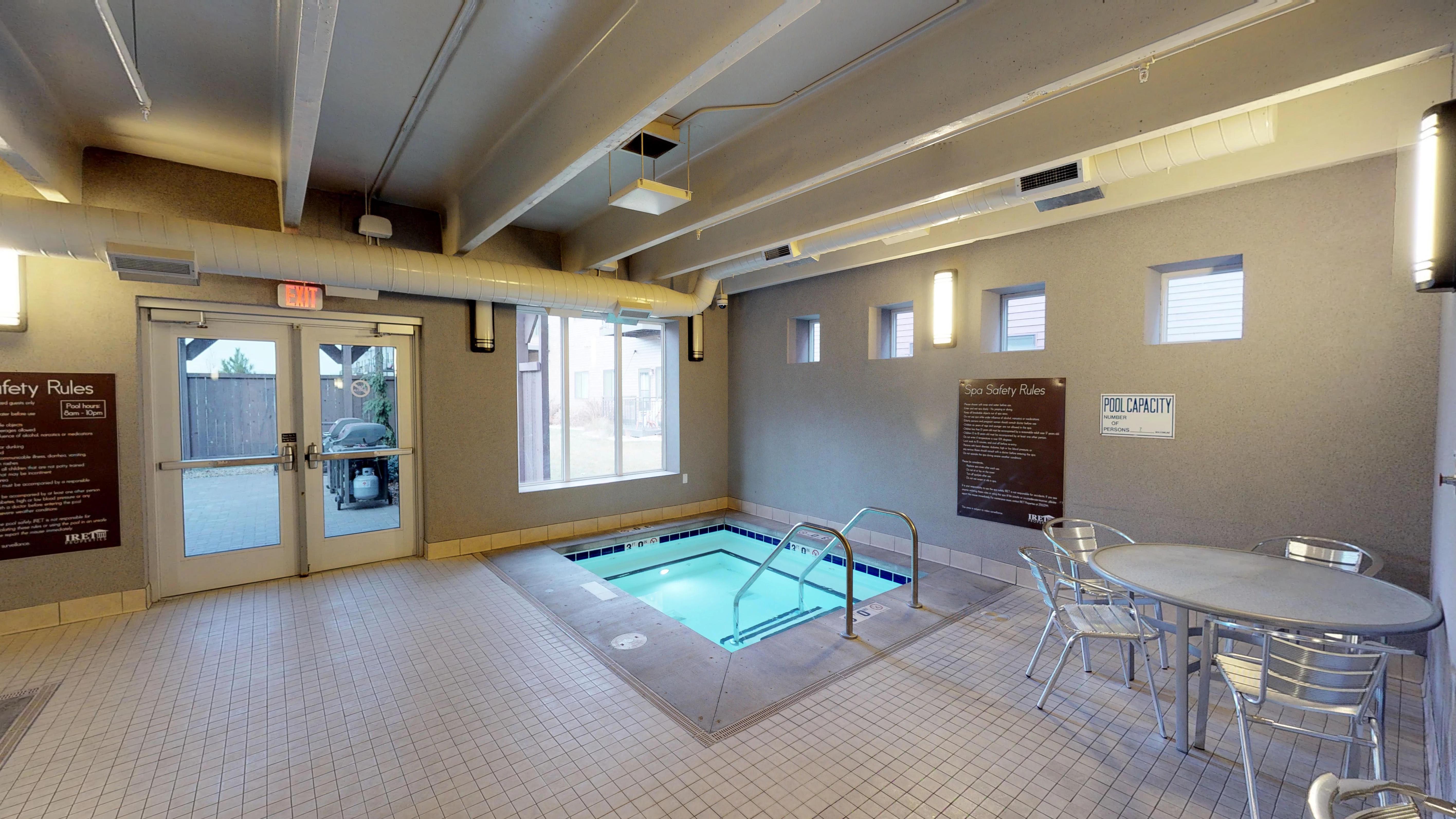Image of the indoor hot tub in the corner with doors to the community grilling area to the left and a nearby table and chairs available for use.